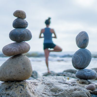 Beautiful girl tree pose yoga by the ocean with stacking rocks